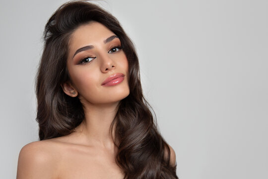 Portrait Of A Brunette With Curly Shiny Hair And Makeup. Gray Background