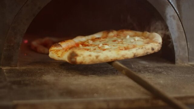 Chef baking Neapolitan pizza in a special oven with high temperature, rotation on a special stick. Professional pizza maker cooking Napoletana pizza.