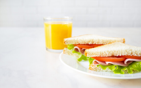 Sandwiches and orange juice on white table. European breakfast