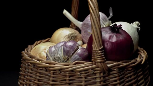 Composition of vegetables, rotation of a basket with onions and garlic on a black background