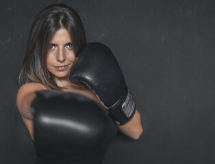 a boxer girl looking straight ahead, in attack and defense position. she has black gloves. the background is dark gray. her light skin stands out against the background.