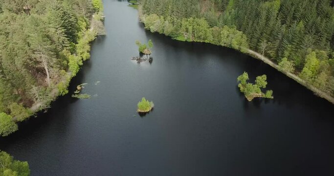 4k aerial footage of Glencoe Lochan showing lochan, surrounding forest, Pap of Glencoe mountain and Loch Leven behind. Cloudy day in springtime.
