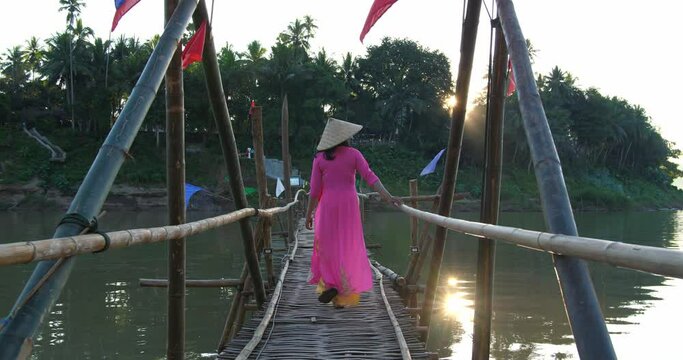 Vietnamese Girl In Traditional Dress Walking On Bamboo Bridge Cross River
