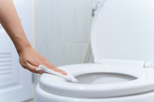 close up hand cleaning Toilet seat by a wet wipe with alcohol spray in public restroom for coronavirus prevention and hygiene before using