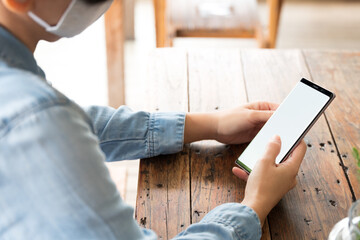 Close up Asian woman's hand holding smartphone with white blank screen, tabbing with thumb, scrolling, sitting at wooden table in beautiful cafe. Social media and lifestyle concept. Mock up.