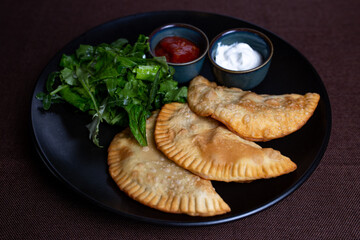 appetizing fried chebureks on a black plate with greens.