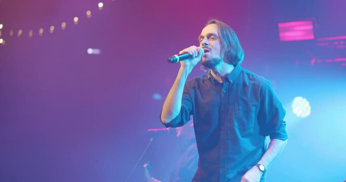 Side view portrait of a man singing to microphone on light background. Stylish cool guy performing concert on stage. Music and concert concept.