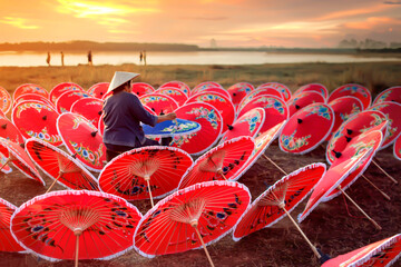 Old Asian woman is painting a colorful gathering by the lake at sunset.