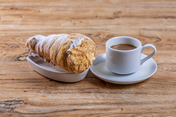  A cup of coffee next to delicious aromatic puff pastry cone with protein cream