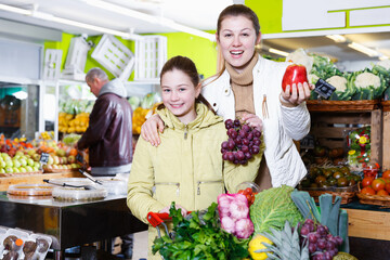 Portrait of cheerful young mother with daughter shopping together in fruit market