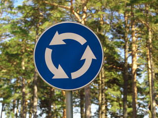 Road sign - a circular movement, against the background of trees. - obrazy, fototapety, plakaty