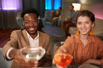 Portrait of elegant mixed-race couple enjoying dinner with friends indoors and toasting to camera