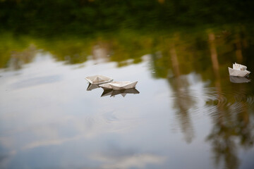 small paper boats in water with sky reflection
