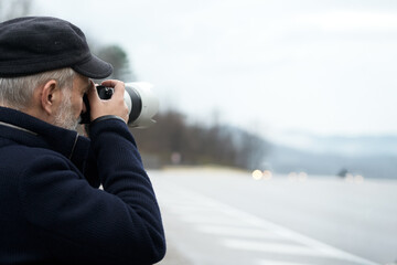 An adult gray-haired man with a camera on a mountain road in foggy inclement weather. Copy space. Selective focus.