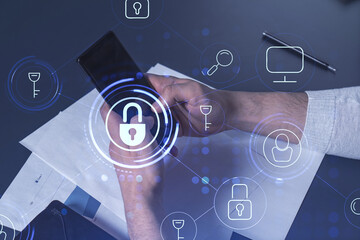 A programmer is browsing the Internet in smart phone to protect a cyber security from hacker attacks and save clients confidential data. Padlock Hologram icons over the typing hands.