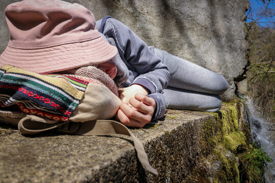Young woman in casual outfit laying on the backpack near the waterfall in the nature and rest from hiking.
Teenage girl sleeping outdoors  on a concrete surface.
