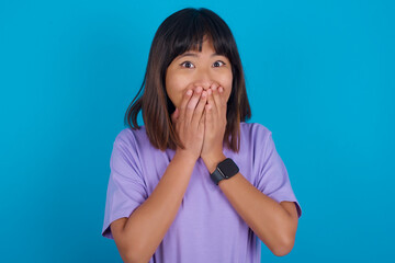 Vivacious young beautiful asian woman wearing purple t-shirt against blue wall, giggles joyfully,...