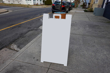 Blank white sandwich board on a sidewalk near houses on a city street