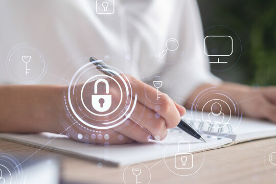 Businesswoman is taking notes of clients needs to protect cyber security from hacker attacks and save clients confidential data. Padlock Hologram icons over the typing hands. Formal wear