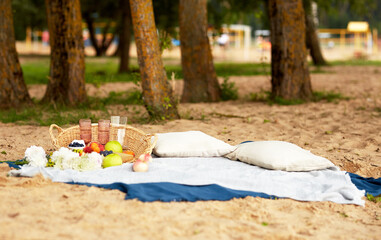 Picnic on the Beach. Blankets and pillows are spread out on the sand. Basket with berries, fruits and wine glasses on a Plaid. Flowers. Food And Drink Conception