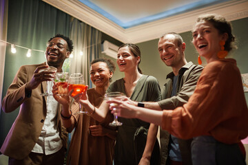 Diverse group of cheerful young people holding glasses and looking at screen while enjoying online party with friends