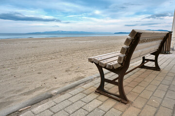 Fototapeta premium Great sea view, and beach together with wooden bench and its metal side exposed to corrosion and remainings of corrosion. Magnificent sky background. Street bench standing on cobblestone pathway.
