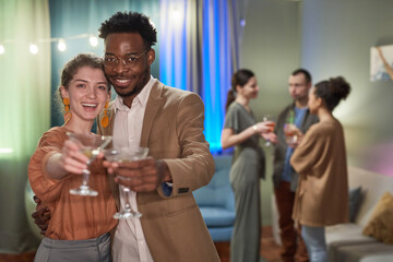 Waist up portrait of elegant young couple looking at camera and clinking glasses while enjoying party at home, copy space