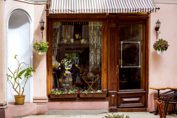 facade of a retro cafe with a large window and a wooden door with glass at the entrance, a table with chairs and decorative flowerpots with flowers and a plant with wall street lights, nobody.