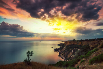 Dramatic sunset at cape Fiolent with bushes grass and rocks at foreground.