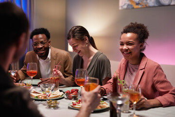 Diverse group of young people at dinner table laughing happily while enjoying party at home