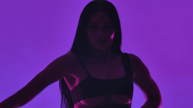 Silhouette of sexy brunette woman with long hair in black leather lingerie is sensually dancing in dark studio with purple lights. Close up. Slow motion.