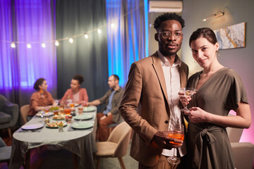 Waist up portrait of mixed-race young couple looking at camera during dinner party with friends, copy space