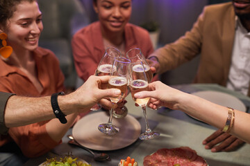 Close up of young people clinking glasses over table while enjoying dinner party with friends