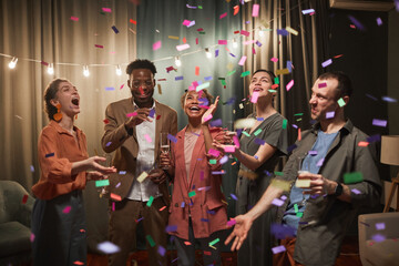 Diverse group of young people dancing under confetti shower while enjoying party with friends indoors