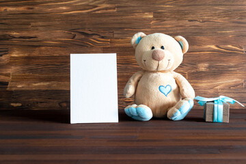 Little teddy bear toy with gift box on wooden table with copy space. Baby shower, accessories, stuff, present for boy child first year happy birthday, first newborn party background