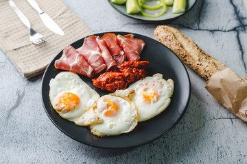 Top angle view on sunny side up eggs prosciutto coppa Capocollo dry meat and homemade ajvar paprika salad on the table as dinner or breakfast meal