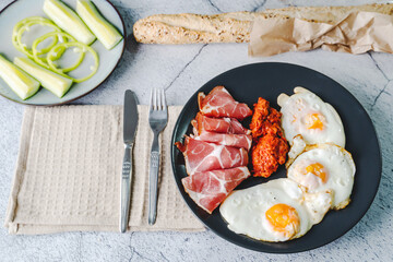 Top angle view on sunny side up eggs prosciutto coppa Capocollo dry meat and homemade ajvar paprika salad on the table as dinner or breakfast meal