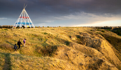 Medicine Hat Alberta Canada, May 13 2021: A family walks outdoors along a hiking trail in Seven Persons Coulee by the Sammis Tepee at sunset. - obrazy, fototapety, plakaty