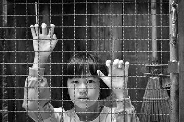 Child girl behind the fence, hand holding steel mesh, black and white toned photo.