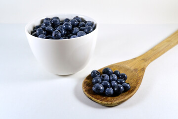 Healthy routine with a wooden spoon and a bowl of fresh blueberries on a white background.