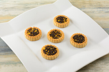 Citrus tartlet cookies with cocoa and orange sprinkles on top on white dessert plate