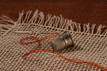 Needle with brown thread and steel thimble on natural linen texture for background. Close. - obrazy, fototapety, plakaty