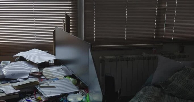 A pan shot of a office with a man working in front of two screens. In the right side of the office ther is a futon for sleep