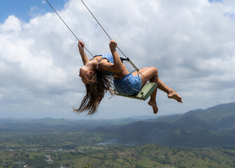 Young woman on the rope swing with sky and mountains background. Concept of freedom and happiness 