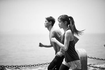 young asian man and woman running outdoors on beach, black and white