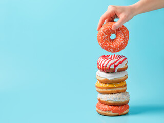 Stack of assorted donuts and one donut in female hand on blue background. Many colorful glazed...
