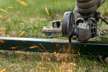 Close-up on the sides fly bright sparks from the angle grinder machine. A young male welder in a ...