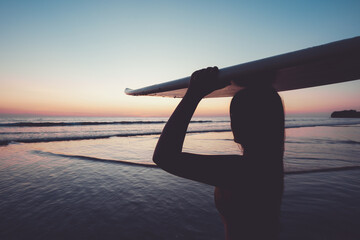 Silhouette of beautiful sexy surfer female with surfboard on the sandy beach at sunset. water...