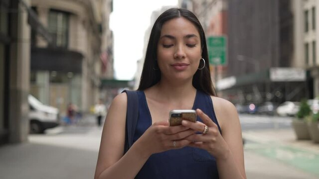 Young Latina Hispanic woman in city walking street texting on cellphone