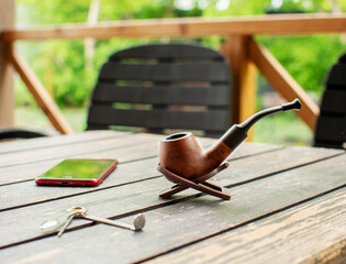 Smoking pipe, telephone, tamper on a crafty brown table.